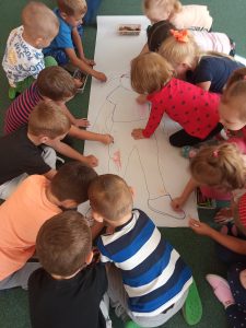 Dzieci z grupy II "Kotki" codziennie wspólnie i radośnie się bawią. Dzisiaj utrwalały części ciała i kolorowały ubranie postaci na dużym arkuszu papieru. 