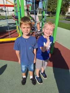 Dwóch chłopców uśmiecha się do zdjęcia na placu zabaw.