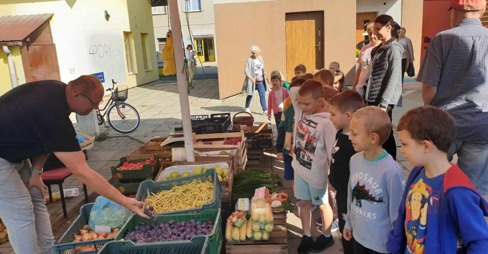 Pan sprzedawca wskazuje warzywa i owoce, a dzieci je nazywają.