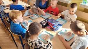Dzieci przy stole piszą literę A, na tackach z piaskiem.
