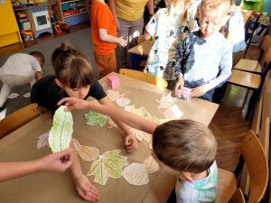 Dzieci ozdabiają szary papier jesiennymi liśćmi.