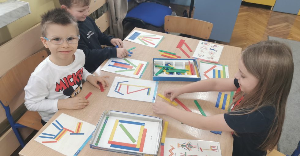 Zabawy Patyczakami - chłopcy układają z kolorowych patyczków wzór z wylosowanej planszy