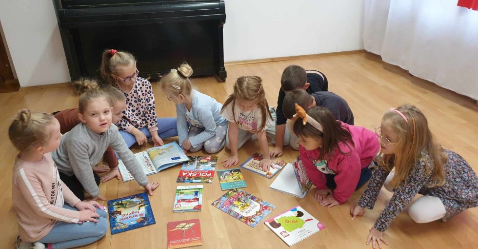 Dzieci siedzą na dywanie wokół książek z legendami polskimi.