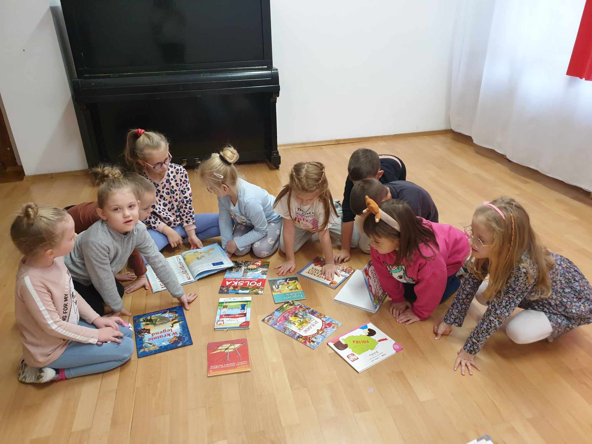 Dzieci siedzą na dywanie wokół książek z legendami polskimi.