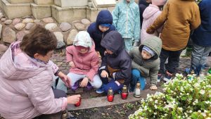 Dzieci z pomocą pani zapalają znicze pod pomnikiem nieznanego żołnierza.