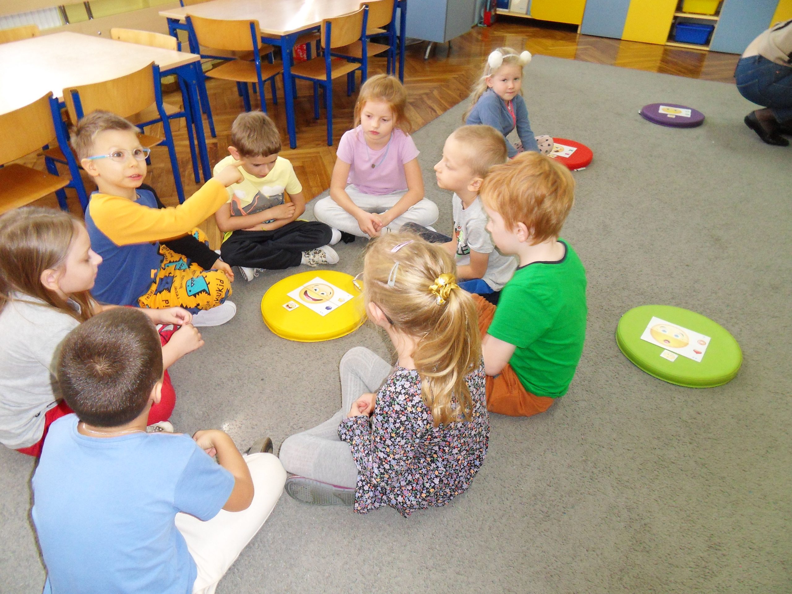 grupa dzieci siedzi wokół emotki z uśmiechem i kolejno opowiadają dlaczego wybrały taki symbool.