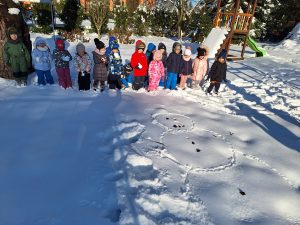 Dzieci pozują do zdjęcia z narysowanym na śniegu bałwanem.