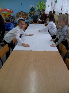 Grupa dzieci nakrywa stół obrusami.