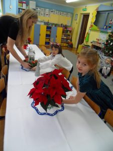 Dwie dziewczynki pomagają p. Sylwii ustawiać kwiaty i stroik na stole.