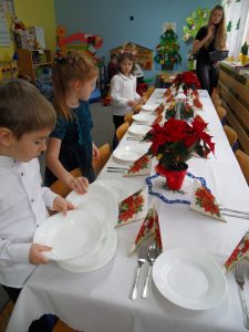 Dwie dziewczynki i chłopiec układają na stole talerze.