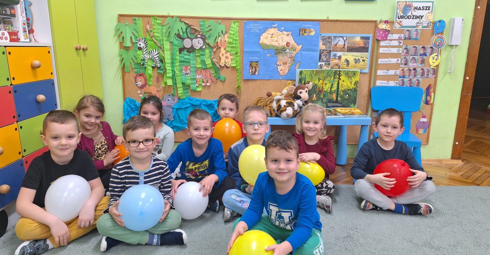 Dzieci pozują do grupowego zdjęcia, trzymając w rękach po balonie.