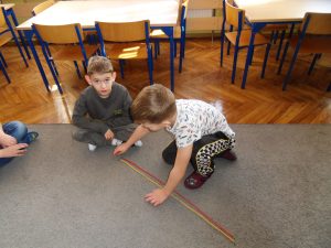 Dzieci pracuj w parach i sprawdzają , czy kolorowe sznurówki ułożone na dywanie, maja taka samą długość.
