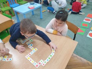Hubert i Zuzia grają przy stoliku w domino z figurami geometrycznymi.
