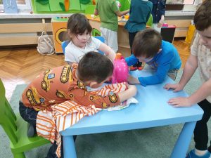 Troje dzieci bawi się w krawców, używając zabawkowej maszyny do szycia.