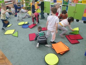 Dzieci z grupy czwartej segregują na dywanie figury geometryczne.