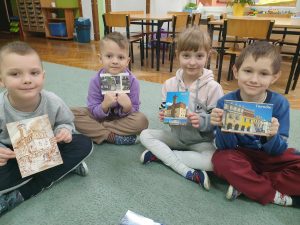Czworo dzieci pozuje do zdjęcia z pocztówkami przedstawiającymi najważniejsze miejsca w Tarnowie.