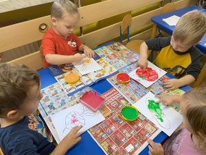 dzieci przy stole farbami malują swoimi palcami narysowane na kartkach warzywa 