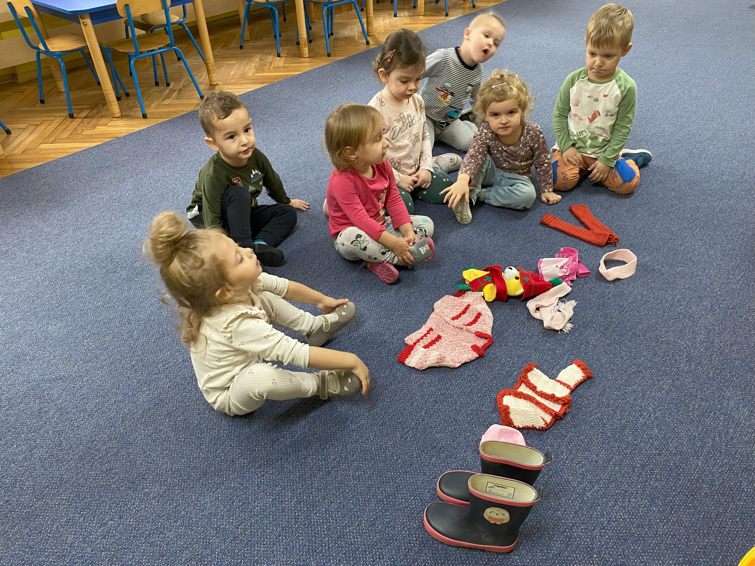 dzieci siedzą na dywanie wśród rozłożonych ubranek dla lalek