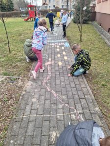 Dzieci malują kredą w ogrodzie przedszkolnym.