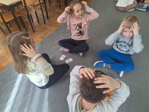 Czwórka dzieci siedzi na przeciw siebie. Między nimi leżą karteczki z literami.