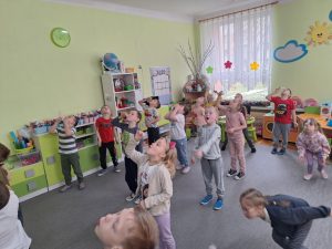 Grupa dzieci dmucha w piórka próbując je utrzymać w powietrzu.
