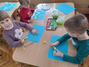Dwoje dzieci przykleja zielone paski papieru - łodygi. Jeden chłopiec maluje śnieg patyczkiem higienicznym.