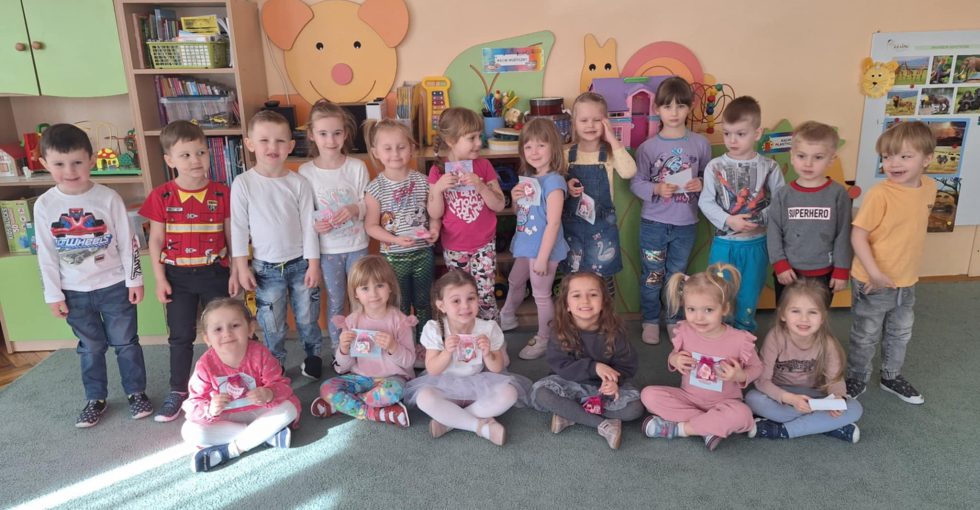 Dzieci z grupy drugiej pozują do zdjęcia z okazji Dnia Kobiet. Dziewczynki trzymają w rękach upominki.