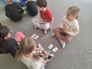 Czwórka dzieci siedzi na przeciw siebie. Między nimi leżą karteczki z literami.