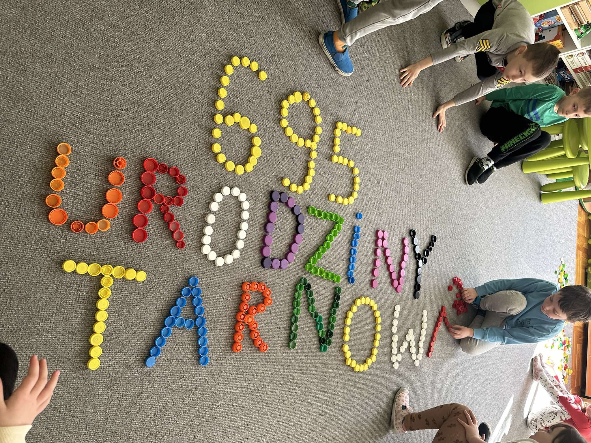 Zdjęcie przedstawia kolorowy napis, utworzony z zakrętek- 695 Urodziny Tarnowa.
