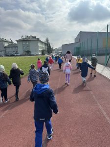 Dzieci idą wzdłuż bieżni sportowej na boisku szkolnym.