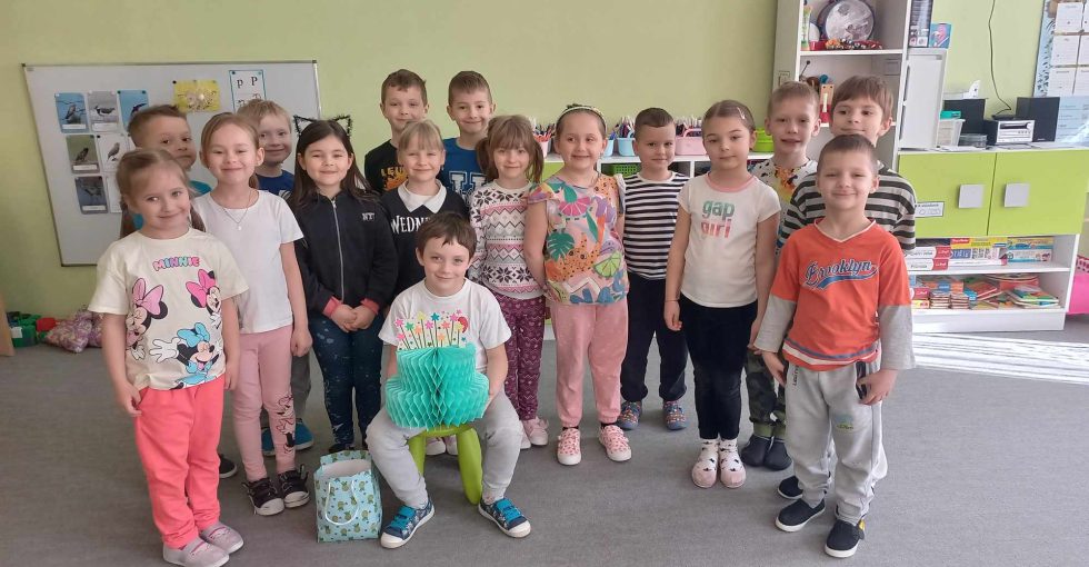Dzieci pozują do wspólnego zdjęcia.Solenizant siedzi na krześle. w rękach trzyma papierowy tort.