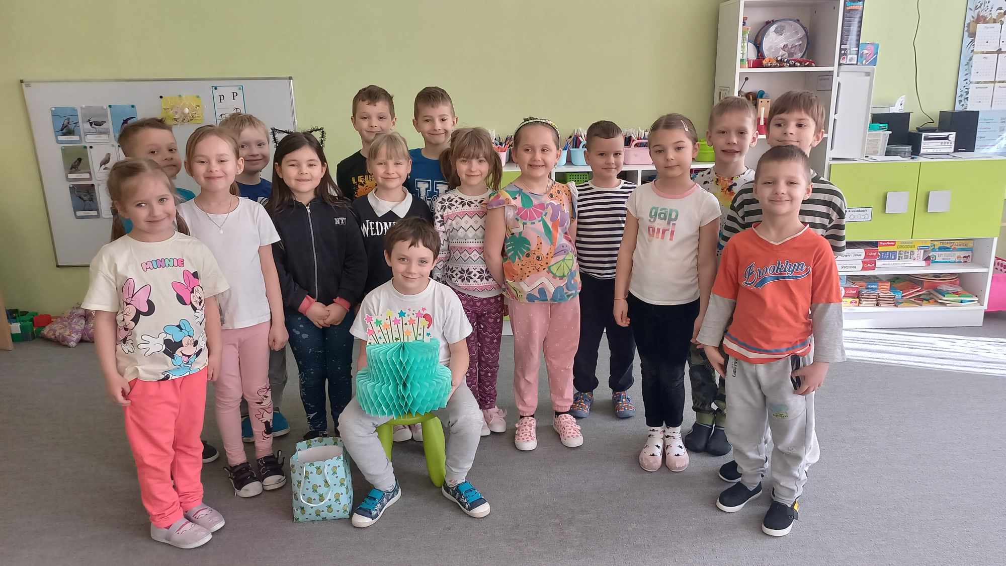 Dzieci pozują do wspólnego zdjęcia.Solenizant siedzi na krześle. w rękach trzyma papierowy tort.