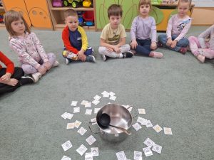 Dzieci siedazą w kole. W środku stoi garnek z chochlą. Dookoła niego leżą emblematy z pogodą.