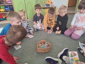 Dzieci siedzą na dywanie. Trzymają karty przedstawiające cechy poszczególnych pór roku.