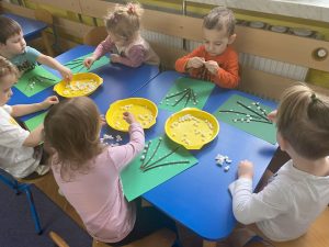 dzieci do gałązek przyklejonych na zielonych kartkach przyklejają białe kuleczki zrobione z waty