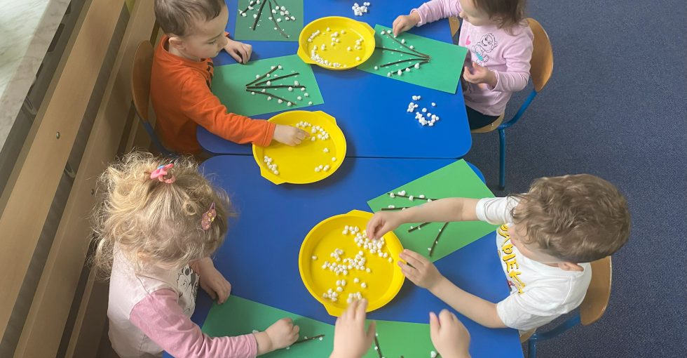 dzieci do gałązek przyklejonych na zielonych kartkach przyklejają białe kuleczki zrobione z waty