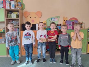 Chłopcy pozują do zdjęcia. Dwóch z nich trzyma koszyczek z upominkami z okazji dnia kobiet.