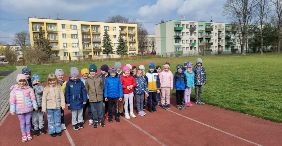 Grupa dzieci stoi na bieżni wokół boiska szkolnego.