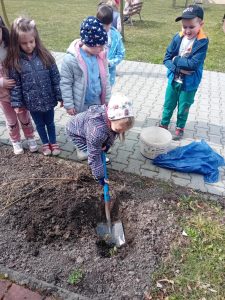 Dziewczynka kopie łopatą dołek w ziemi.
