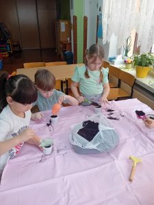 Dwie dziewczynki i chłopiec przy użyciu łopatek wsypują ziemię do plastikowych pojemników.