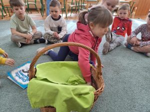 Dziewczynka wkłada rękę do kosz, który jest przykryty serwetą.