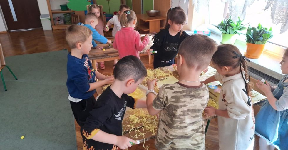 Grupa dzieci pracuje przy stolikach. Wykonują prace techniczną - domki dla Trzech Świnek z bajki.