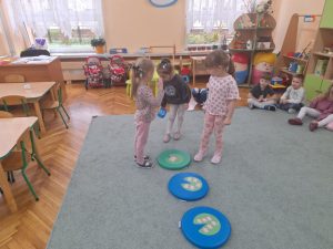 Troje dzieci stoi wokół kolorowych podkładek na których ułożone są liście i kwiaty lilii wodnych. Jedno dziecko trzyma dużą kostkę.