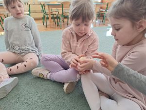 Dzieci siedzą w kole na dywanie, podają sobie jajko z rąk do rąk.