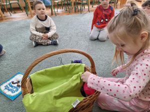 Dziewczynka wkłada rękę do kosz, który jest przykryty serwetą.