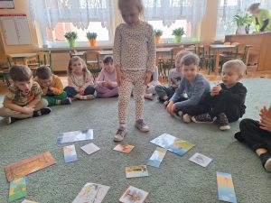 Dziewczynka stoi. Przygląda się obrazkom rozłożonym na dywanie.
