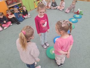 Trzy dziewczynki stoją wokół kolorowych podkładek na których ułożone są liście i kwiaty lilii wodnych.