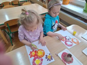 Dwoje dzieci przy stoliku. Wykonują prace plasytyczną - odbijają nacięte rolki po papierze tworząc wiosenne kwiaty.