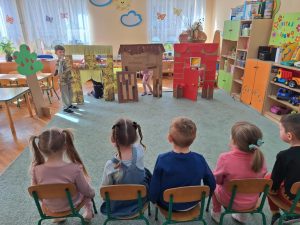 Dzieci siedzą na krzesełkach. Oglądają spektakl o Trzech świnkach w wykonaniu swoich kolegów i koleżanek z grupy.