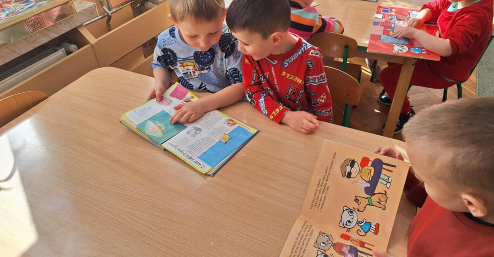 Dzieci siedzą przy stole i oglądają wybrane książki.